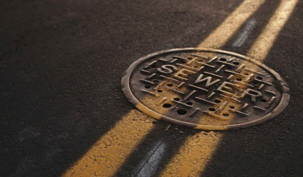 Sewer manhole cover on highway with yellow lines painted overtop.