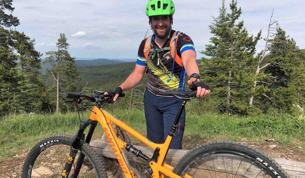 Adam Baxter smiling with his bike next to a trail in Calgary.