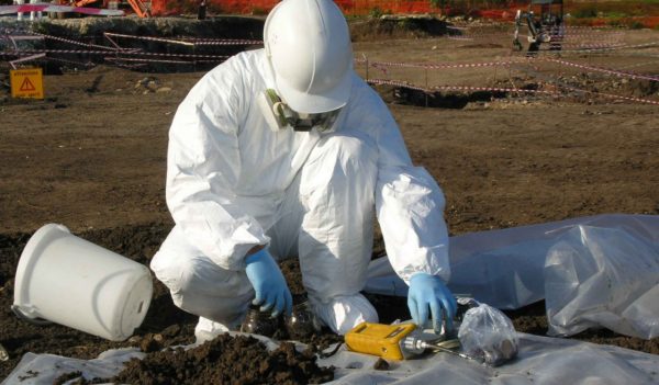 worker in white suit inspecting dirt