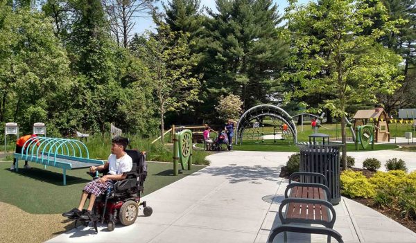 Man in wheelchair in a park with benches and play equipment.